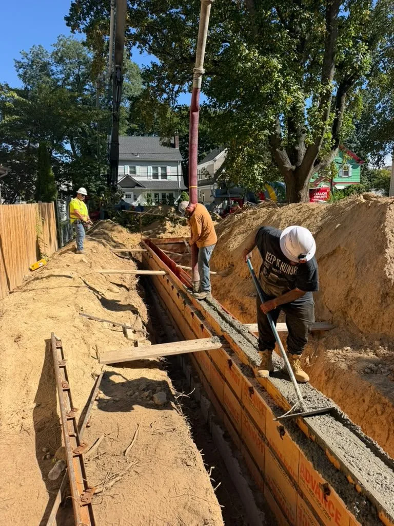 Crew guiding a concrete pump hose into foundation wall forms