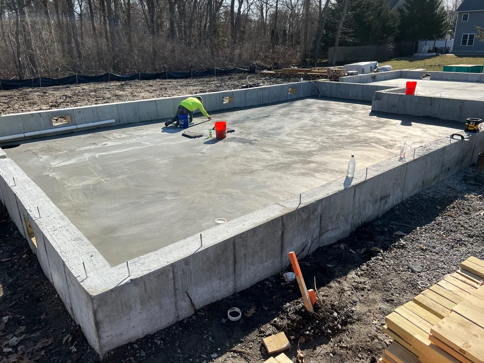 A finisher working a fresh concrete slab inside foundation walls