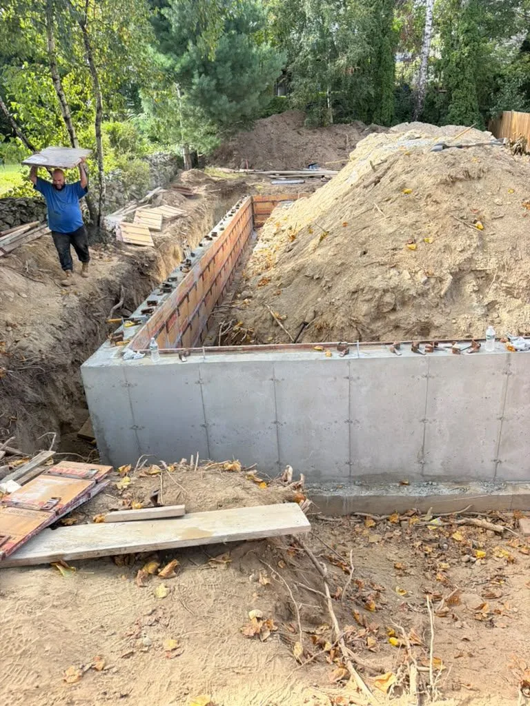 A crew member carrying form panels beside a finished foundation wall