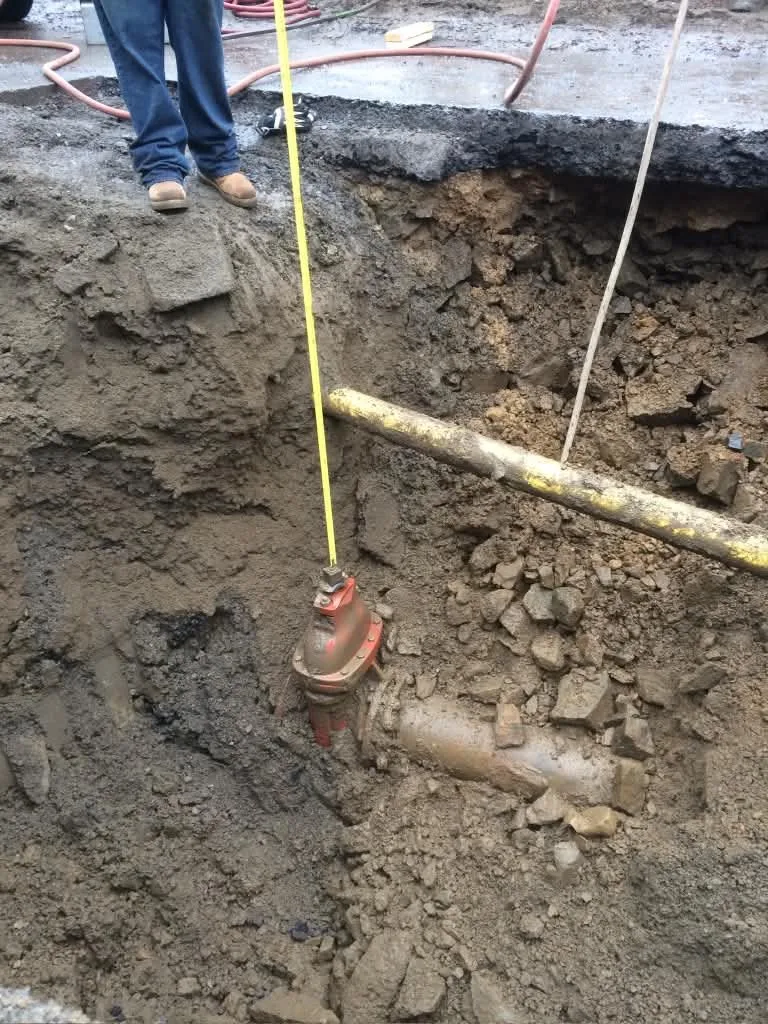 A measuring tape against a sewer pipe connection in an open trench